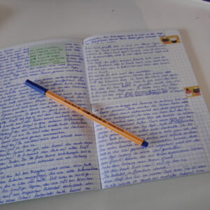 Heft mit handgeschriebenen Text, ein Post it klebt darauf und ein Teil ist mit einem weiteren Blatt überklebt